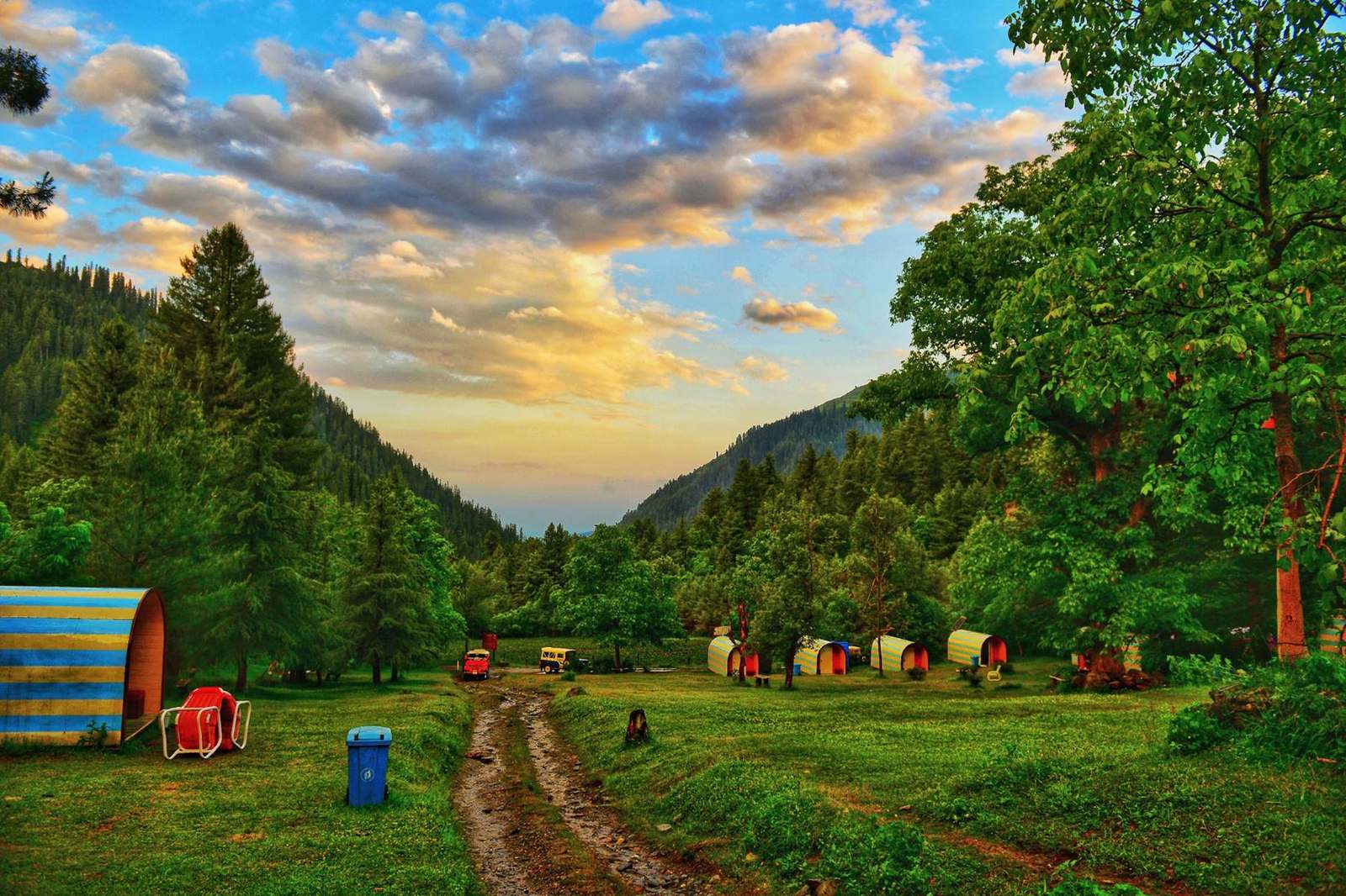 Striped huts in a green clearing in Sharan forest at sunset