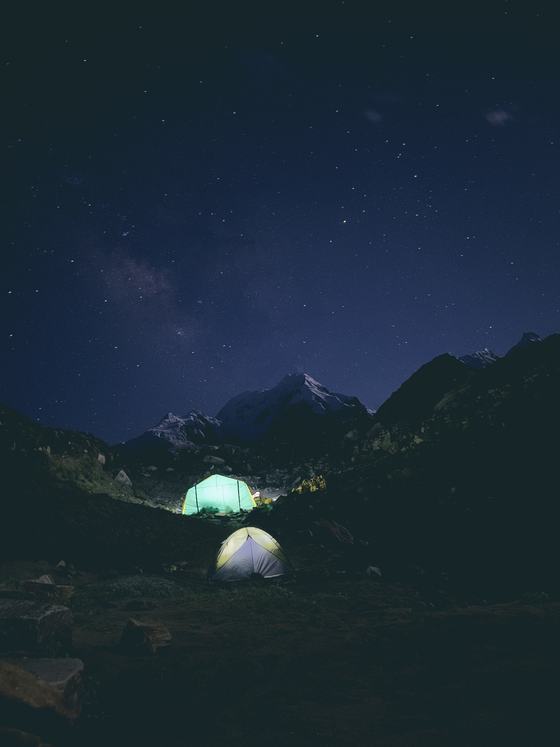 Lit tents under the Milky Way below a snow peak