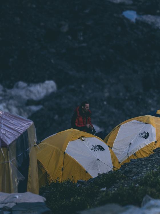 A climber among yellow expedition tents at dusk