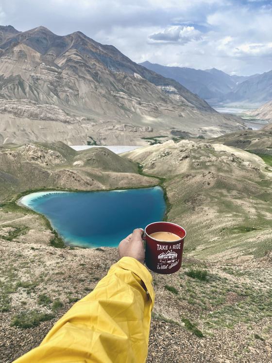 Tea held up above a turquoise high-altitude lake