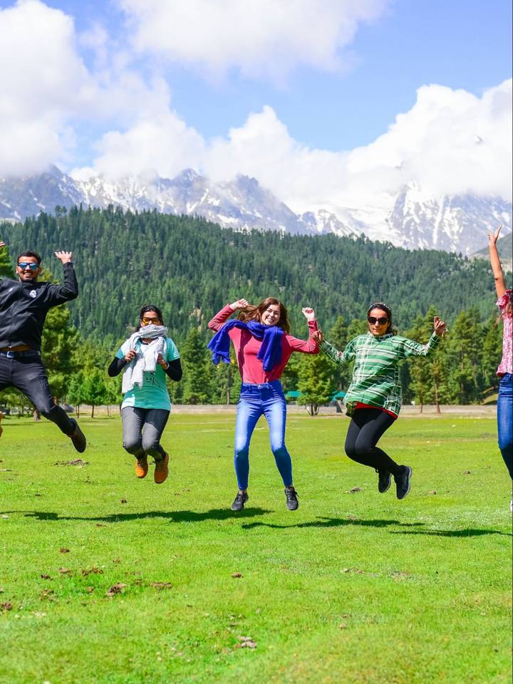 A Travelore group jumping on a meadow below snow peaks