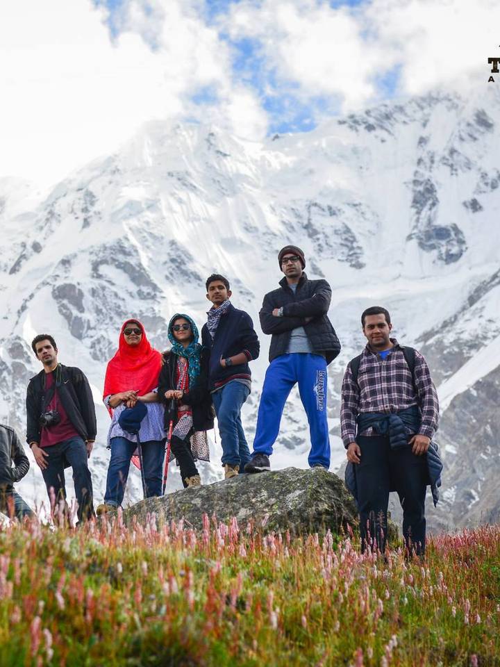 A Travelore group on a rock above wildflowers, with Nanga Parbat behind