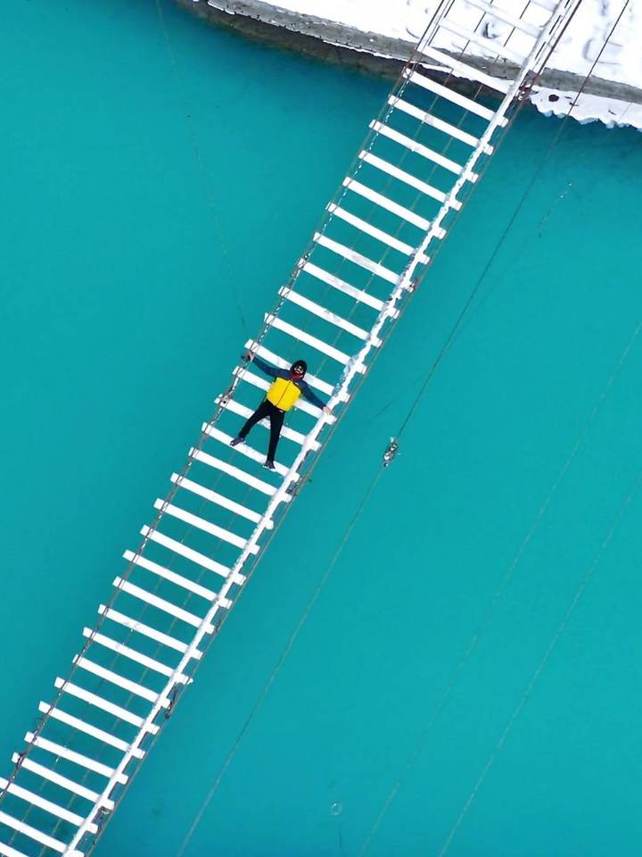 Drone view of a traveller lying on a suspension bridge over turquoise water