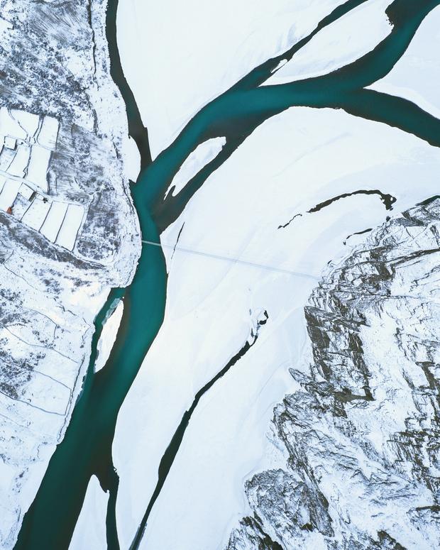 Drone view of a turquoise river braiding through snow