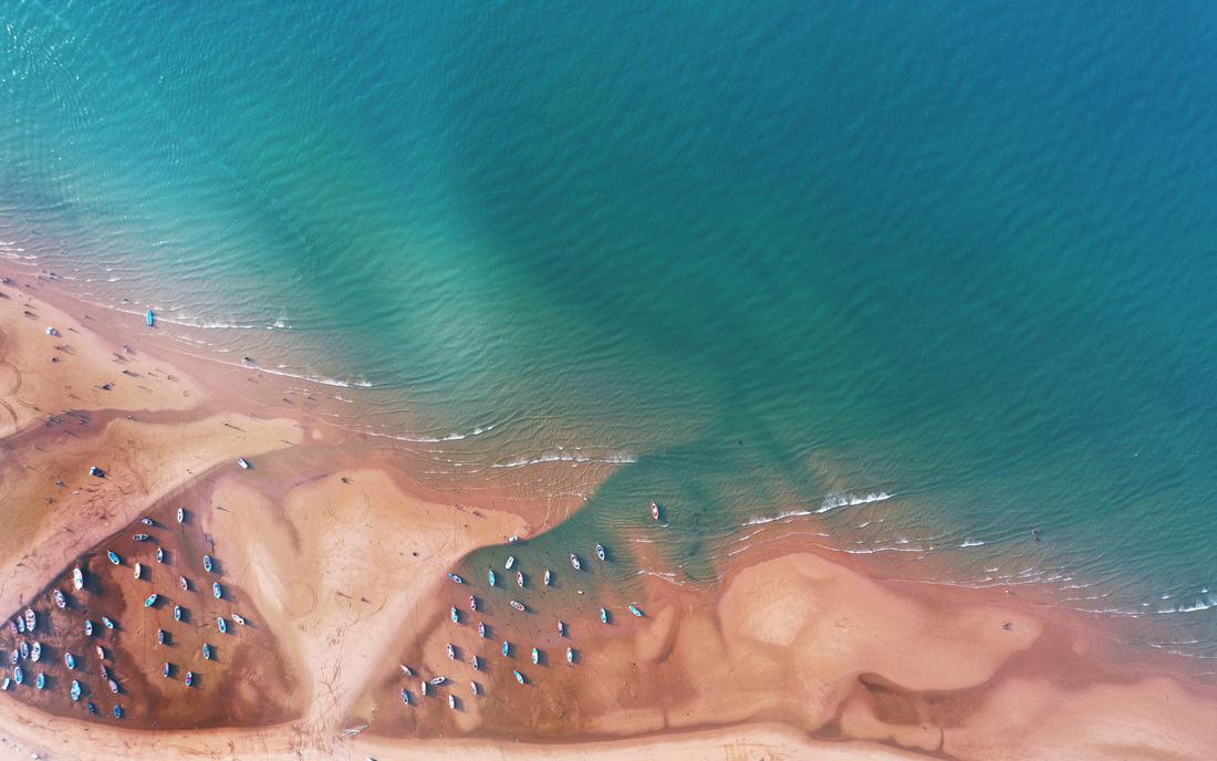 Drone view of fishing boats on a sandbank where the sea meets the shore