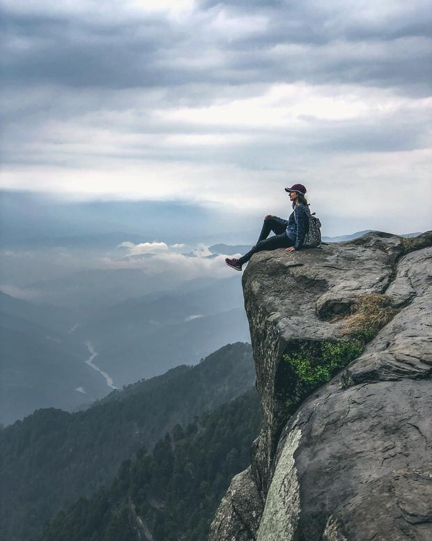 A hiker sitting on the edge of a cliff above cloud-filled valleys
